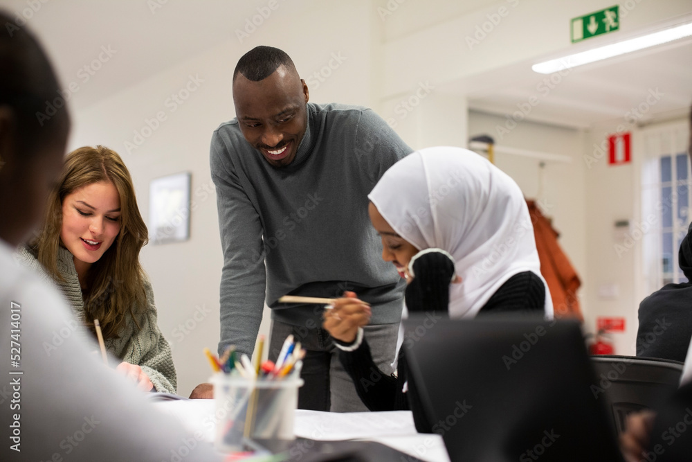 Smiling male teacher talking to students in classroom Smiling male teacher talking to students in classroom