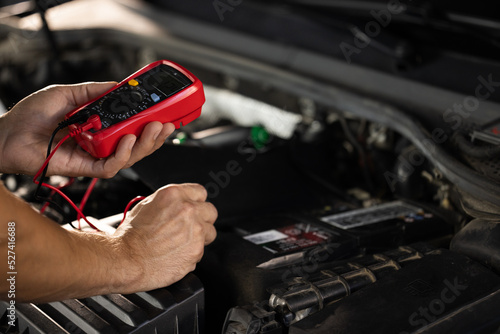 Check battery voltage with electric multimeter. Man using multimeter to measure the voltage of the batteries. Mechanic doing car inspection, he is testing car battery with tester photo