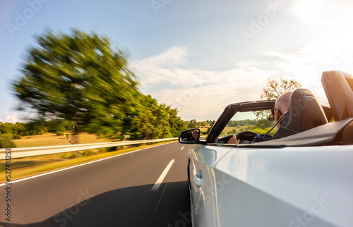 Adult man is driving with convertable car in sunny nature on a bright summer day. wide angle pursuit shot with high speed motion blur © AA+W