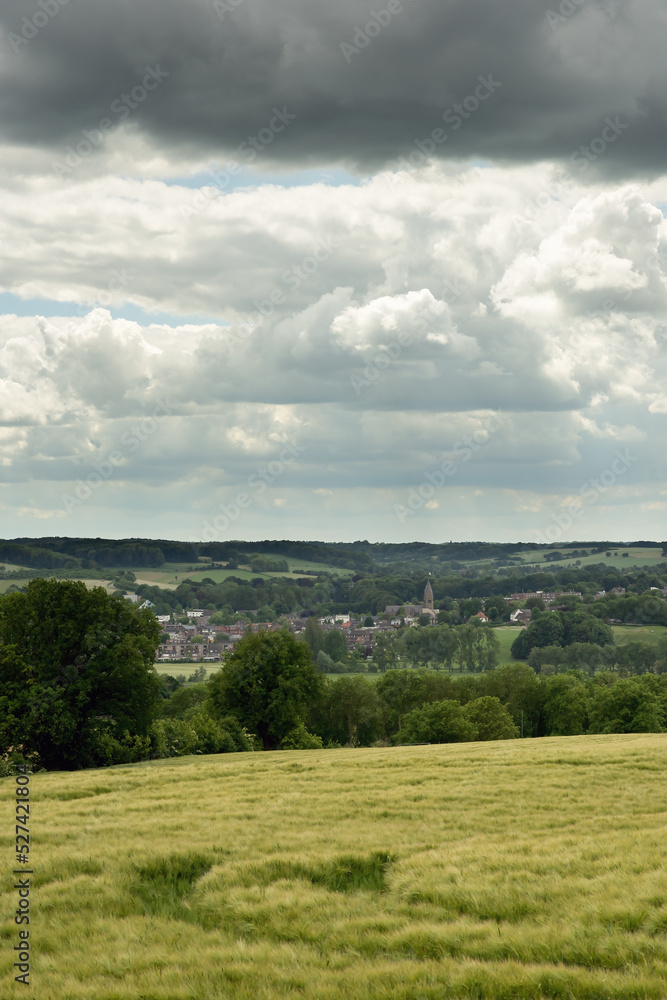 Rolling countryside with a village and church under a cloudy sky.