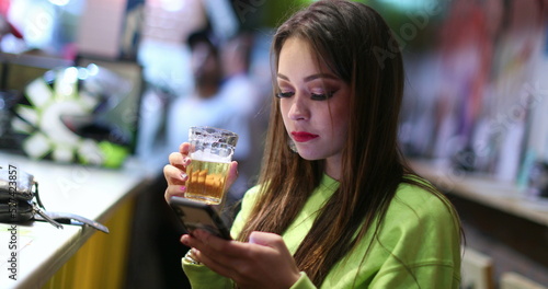 Candid pretty girl at bar drinking beer and checking smartphone