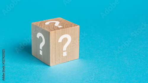 wooden toy cube with white question marks viewed high angle on a blue background