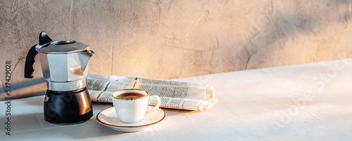 Foto A cup of espresso, a coffee maker and a newspaper in the morning sunlight