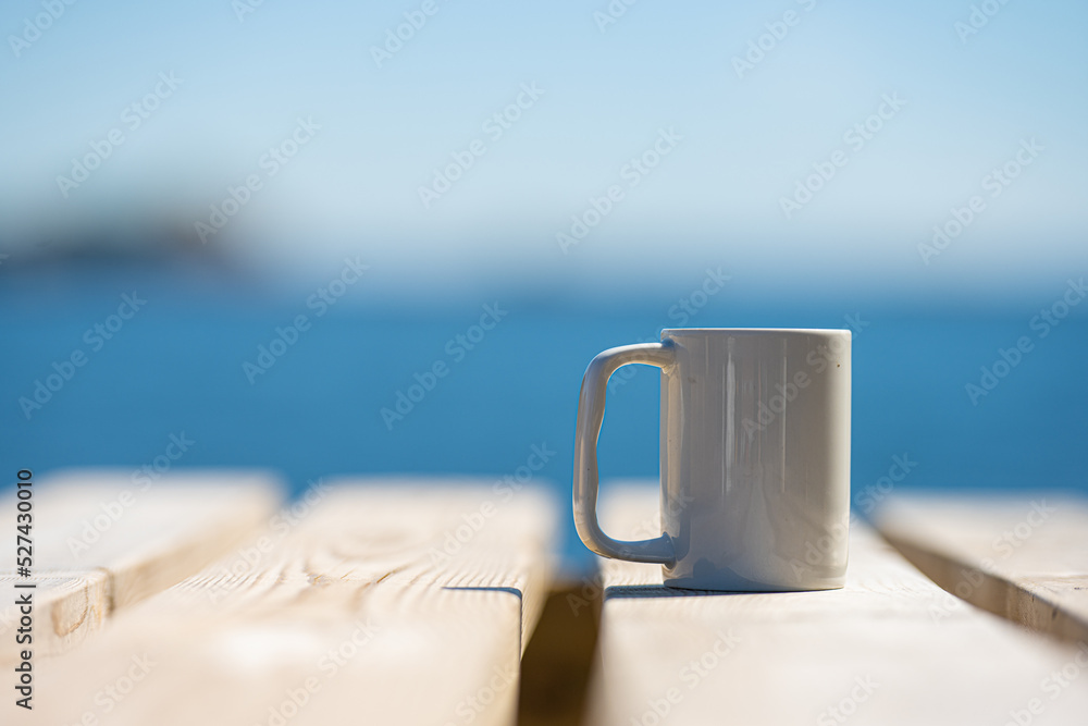 White mug on a wooden table by the sea.