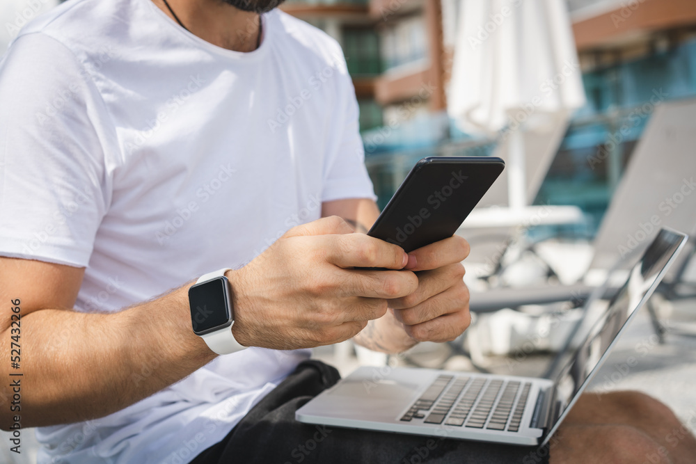 Cropped shot of young man freelancer working using his laptop while sitting at the deck chair near the pool in the hotel Cropped shot of young man freelancer working using his laptop while sitting at the deck chair near the pool in the hotel