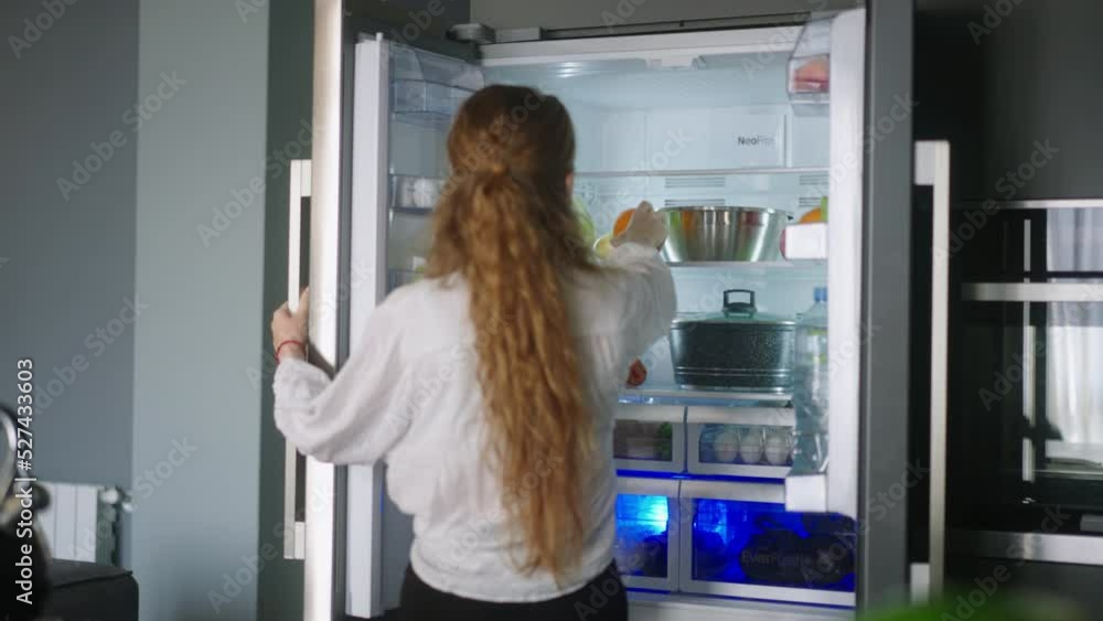Young woman taking an orange from fridge throwing it up. Girl getting a fruit from refrigerator. Female having something healthy for snack. Caucasian woman is about to cut orange. Girl cutting orange Young woman taking an orange from fridge throwing it up. Girl getting a fruit from refrigerator. Female having something healthy for snack. Caucasian woman is about to cut orange. Girl cutting orange
