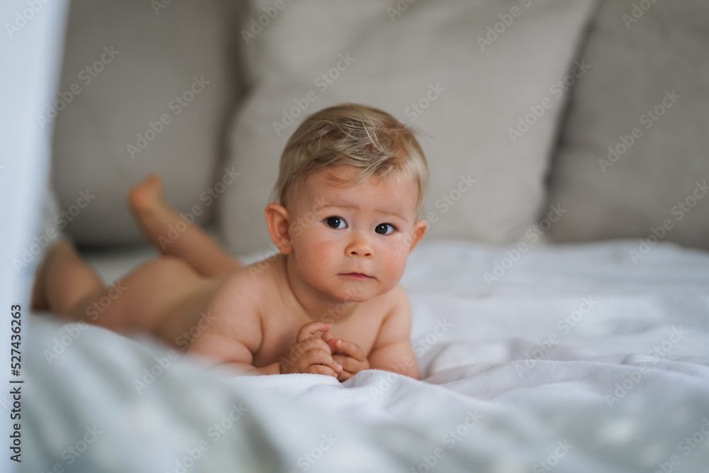 super sweet naked almost one year old happy blond baby boy lying at home on a cozy bed after
