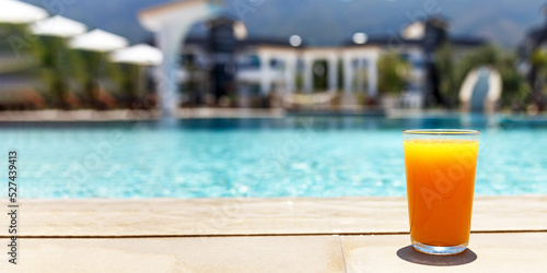 Glass of fresh cool orange juice drink on swimming pool board, summer tropical holiday concept.Banner with copy space