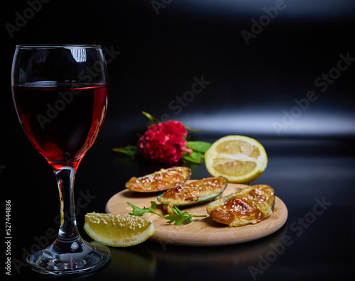 mussels baked delicacy on a round wooden plate with a slice of lemon on a dark background