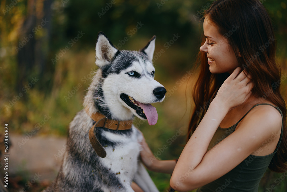 A woman with a husky breed dog smiles and affectionately strokes her beloved dog while walking in nature in the park in autumn against the backdrop of sunset A woman with a husky breed dog smiles and affectionately strokes her beloved dog while walking in nature in the park in autumn against the backdrop of sunset