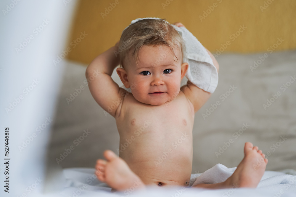 happy cute naked one year old happy blond baby boy sitting at home on a cozy bed after bathing and smiling or flirting into the Camera happy cute naked one year old happy blond baby boy sitting at home on a cozy bed after bathing and smiling or flirting into the Camera
