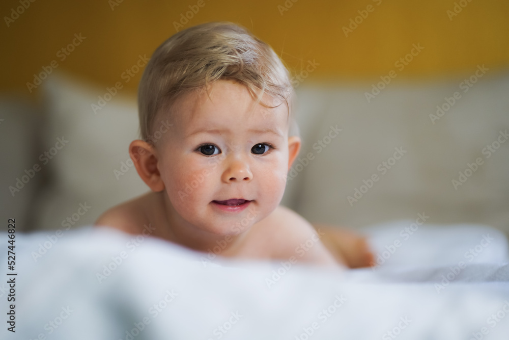 happy cute naked one year old happy blond baby boy sitting at home on a cozy bed after bathing and smiling or flirting into the Camera happy cute naked one year old happy blond baby boy sitting at home on a cozy bed after bathing and smiling or flirting into the Camera