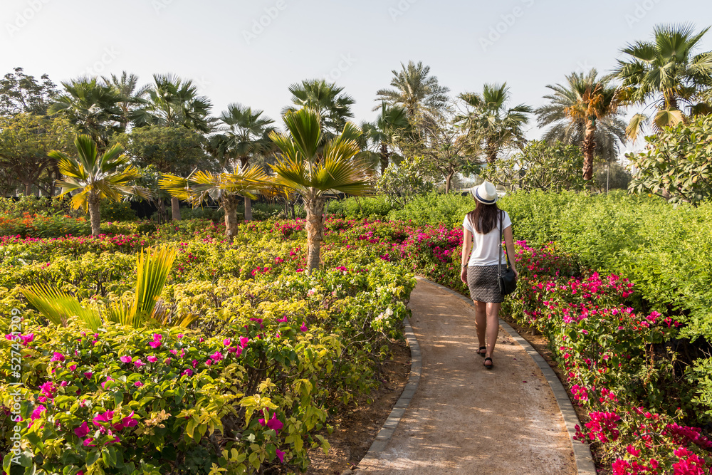 A young caucasian girl tourist in a white hat walks in a botanical garden with exotic plants.