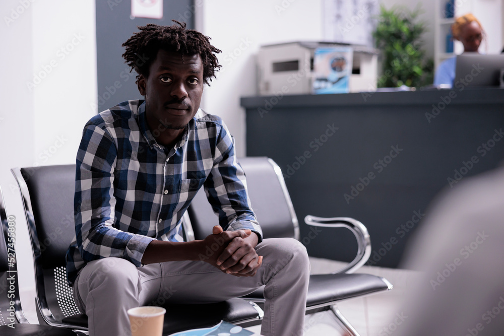 Portrait of male patient sitting in waiting room, having checkup examination appointment with physician to cure disease diagnosis. Young adult in waiting area at hospital lobby before consultation. Portrait of male patient sitting in waiting room, having checkup examination appointment with physician to cure disease diagnosis. Young adult in waiting area at hospital lobby before consultation.