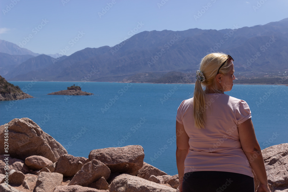 Blonde woman looking a beautiful scenery with a lake and mountains on a sunny day.