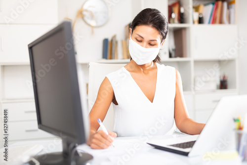 Business woman in protective medical mask using laptop at workplace