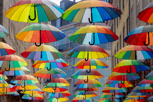 Fototapeta Naklejka Na Ścianę i Meble -  Colorful rainbow umbrella between building above pink street, Small road in city center of Lisbon, Symbol of Gay, Lesbian, Bisexual and Transgender, LGBT community and social movements, Portugal.