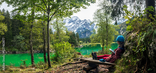 Mid Adult Woman Reading on a Digital tablet Outdoors on a bench near a beautiful Alpine Lake - .Fusine Lakes Italy