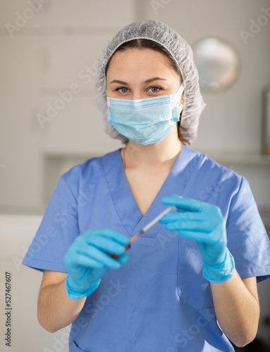 Girl nurse in mask holding syringe for injection in modern clinic