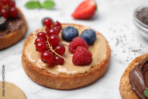 Tasty organic rusk with peanut butter and sweet berries on white marble table, closeup
