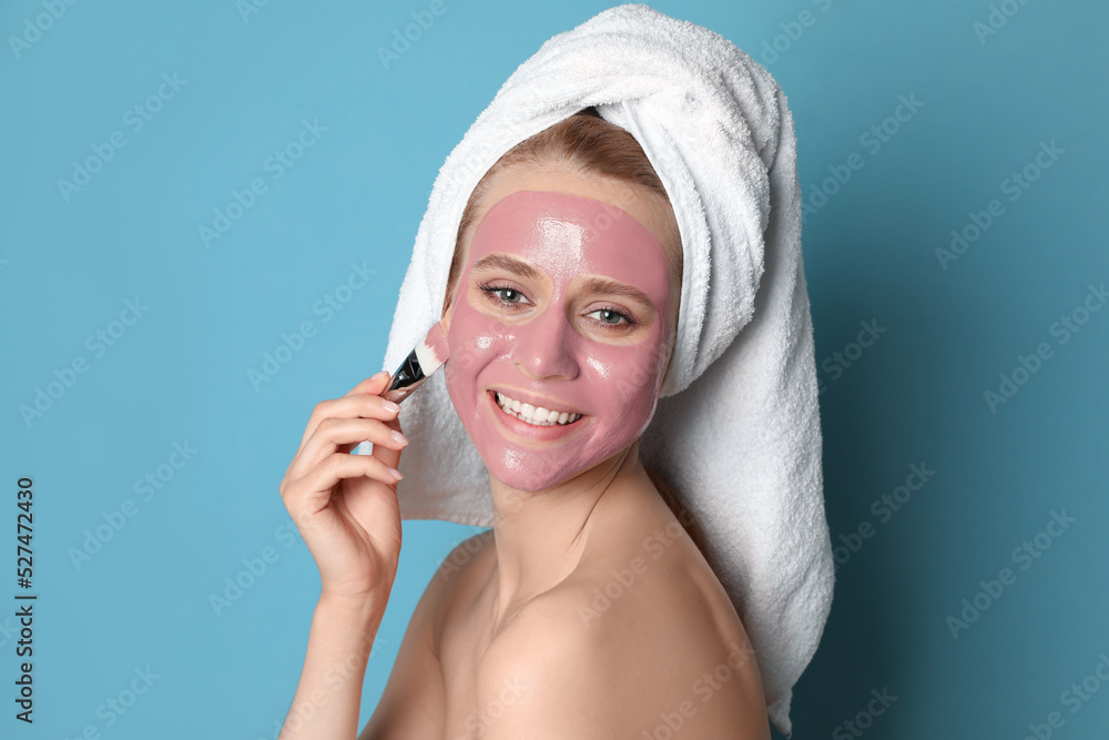 Young woman applying pomegranate face mask on light blue background Young woman applying pomegranate face mask on light blue background