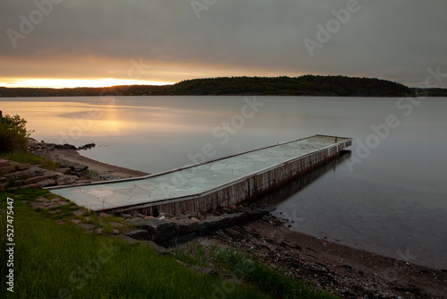 Stone covered jetty by beach and calm water in sunrise ligth at a fjord in southern Norway