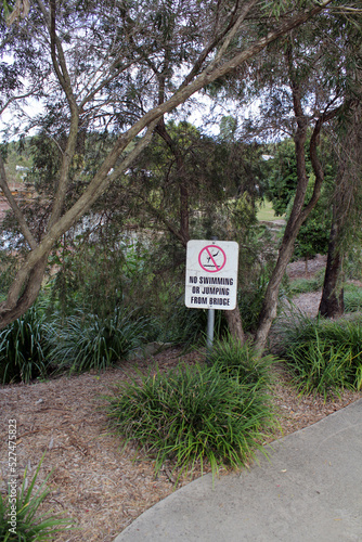 "No swimming or diving from bridge" sign in a park with trees and plants