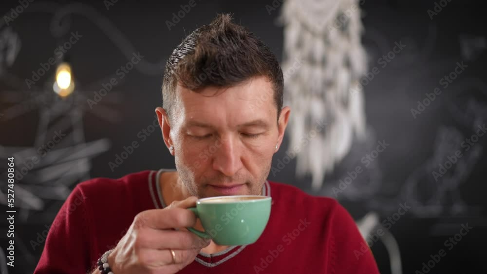Close-up man smelling freshly brewed coffee in slow motion looking at camera with satisfied facial expression. Front view headshot of Caucasian client posing indoors in cafe with tasty hot drink Close-up man smelling freshly brewed coffee in slow motion looking at camera with satisfied facial expression. Front view headshot of Caucasian client posing indoors in cafe with tasty hot drink