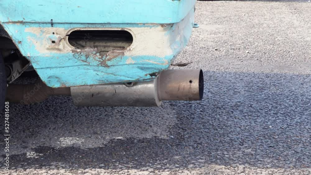 Metal muffler on car on asphalt road. Old resonator on back of blue car