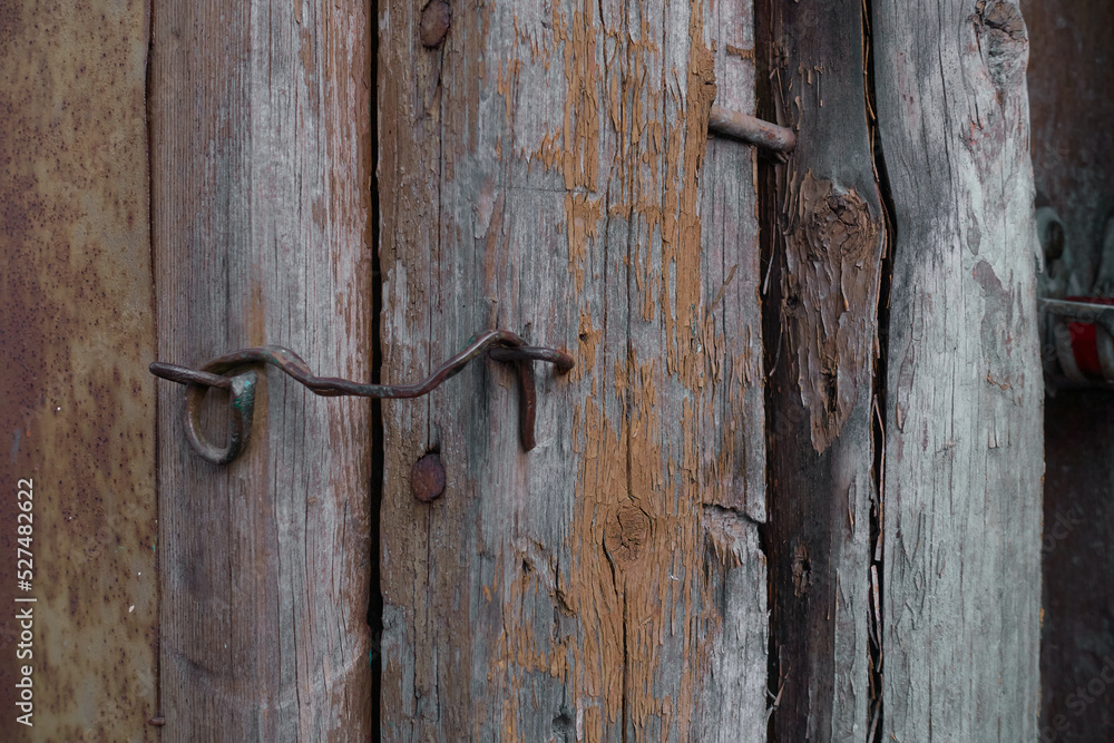 An old brass hook closes a dilapidated door on an old dilapidated wooden shed. The paint is peeling off the boards and rusty nails are sticking out. An old brass hook closes a dilapidated door on an old dilapidated wooden shed. The paint is peeling off the boards and rusty nails are sticking out.