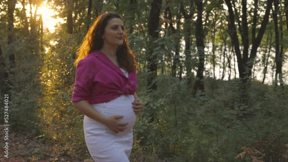 Pregnant mom looking ahead while walking in forest as exercise, sun sets behind Pregnant mom looking ahead while walking in forest as exercise, sun sets behind