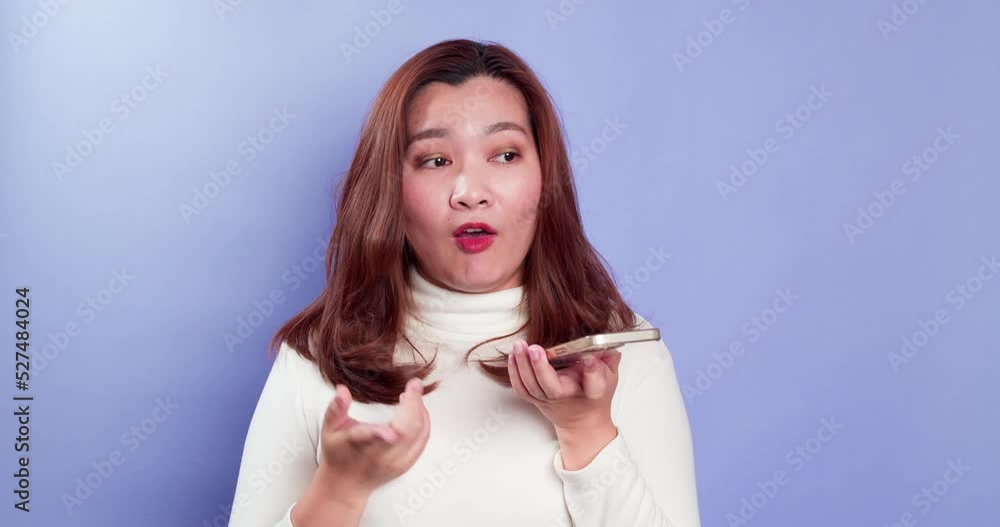 Young Asian women talk on a phone using loudspeaker on technology to network with clients or negotiate deals isolated over a violet background Young Asian women talk on a phone using loudspeaker on technology to network with clients or negotiate deals isolated over a violet background