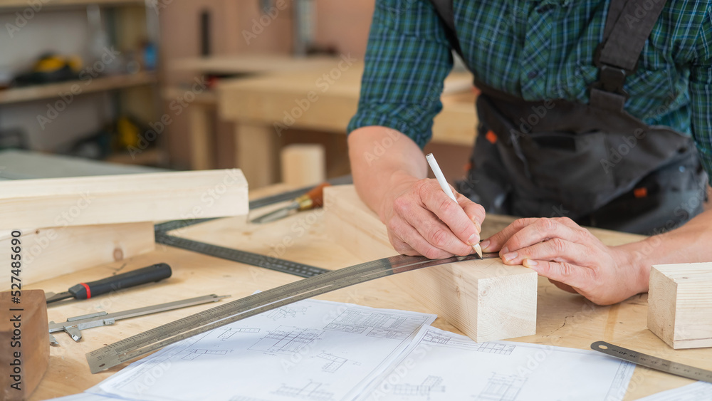 A carpenter measures wooden planks and makes marks with a pencil in a workshop. A carpenter measures wooden planks and makes marks with a pencil in a workshop.