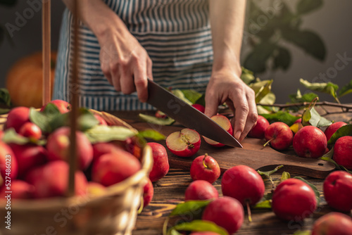 Woman in an apron in the kitchen is cutting appetizing red apples from a fresh harvest. Concept of an autumn cozy atmosphere, cooking dishes from organic healthy apples from own garden