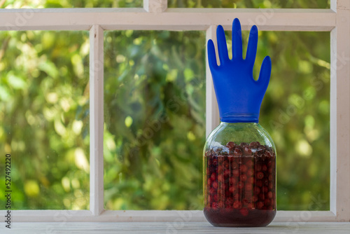Homemade tincture of red cherry in a jar with a glove shaped shutter. Berry alcoholic drinks concept. Homemade red wine made from ripe cherries in glass jar on white wooden window background