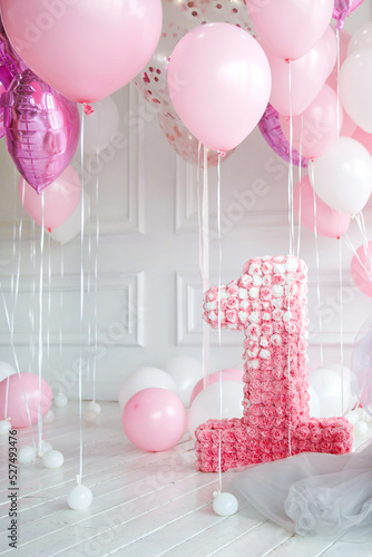 pink helium balloons and number one, on background of white wall and wooden floor. Greeting or invitation card for birthday, anniversary