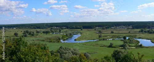Summer landscape with a river flowing in a valley and a blue sky with clouds. Panorama.