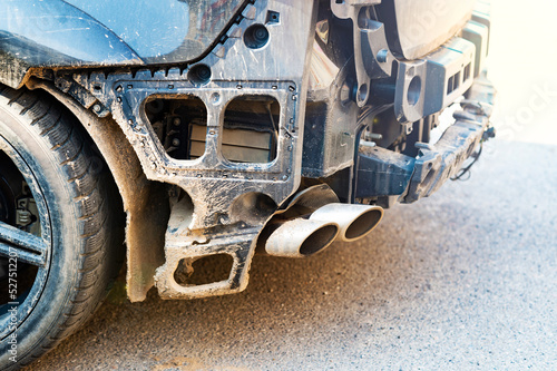 A close-up of the rear view of a black car involved in an accident with a broken bumper and a protruding exhaust pipe. Аutomobile damage from a collision in the city on the road.