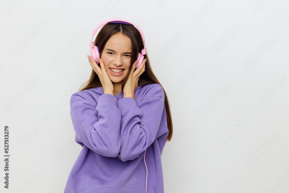 horizontal studio photo of a happy, joyful woman in a purple tracksuit listening to music holding her pink headphones with both hands and smiling broadly looking at the camera horizontal studio photo of a happy, joyful woman in a purple tracksuit listening to music holding her pink headphones with both hands and smiling broadly looking at the camera