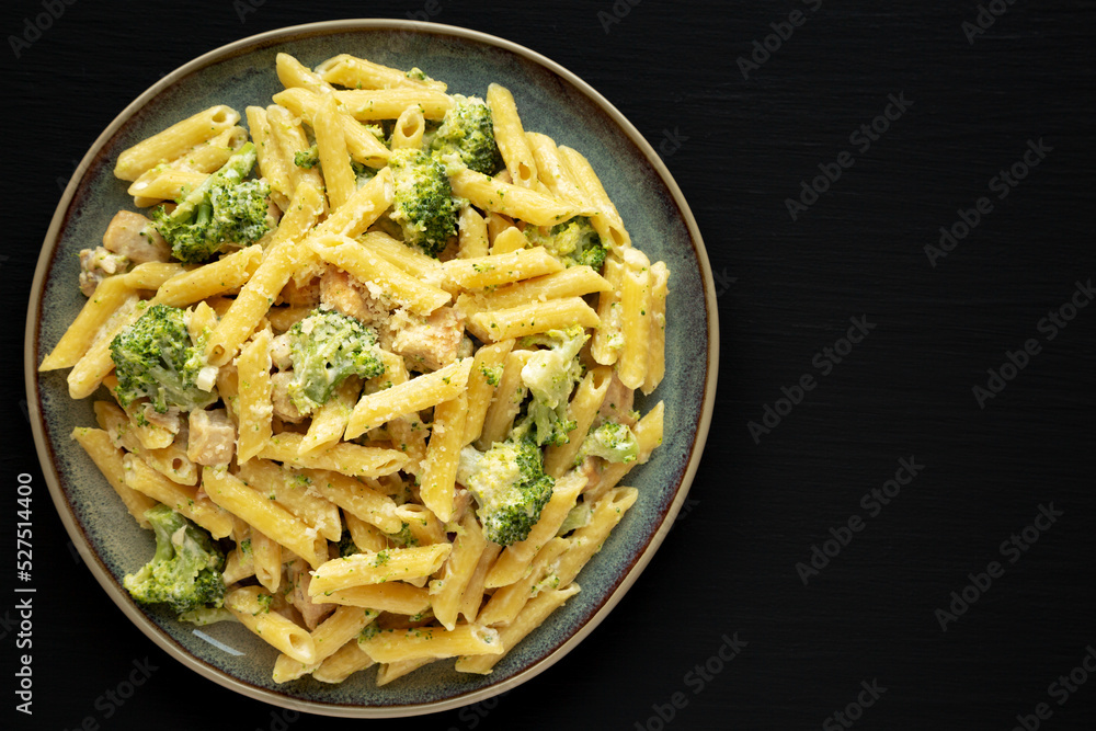 Homemade Penne Alfredo Pasta with Chicken and Broccoli on a Plate on a black background, top view. Overhead, flat lay, from above. Copy space. Homemade Penne Alfredo Pasta with Chicken and Broccoli on a Plate on a black background, top view. Overhead, flat lay, from above. Copy space.
