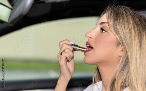 woman painting her lips in a car parked in a city