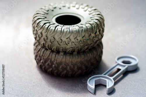 black rubber tire from toy car and plastic gray wrench key isolated on dark structured paper background.tires replacement winter season concept.auto service,vehicle care maintenance.