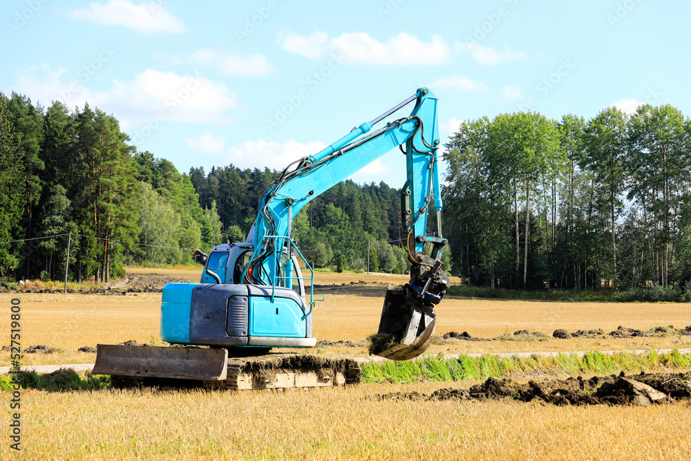 Blue Compact Tracked Excavator at Work Digging a Trench in Field Blue Compact Tracked Excavator at Work Digging a Trench in Field