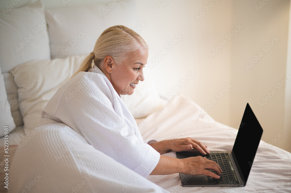 A woman in white robe lying on bed and working on laptop A woman in white robe lying on bed and working on laptop