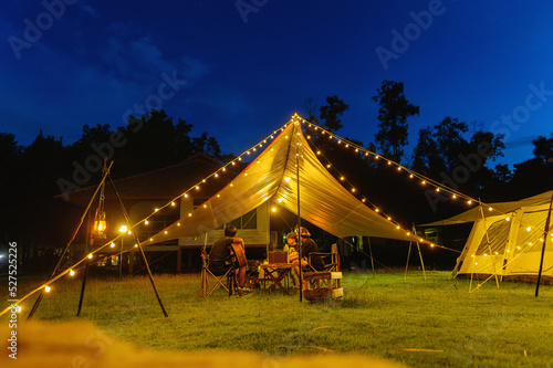 Outdoor camping tent with tarp or flysheet on grass courtyard and warm night light under dark blue sky twilight time, family vacation picnic on holiday relax, Overview of camping of family tourist.