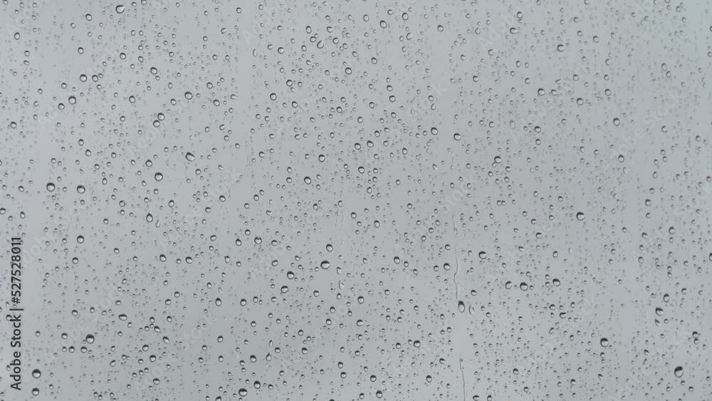 Wet glass. Drops of water on glass. Abstract background. Grey sky. Overcast weather. Water flows. Close-up. Wet glass. Drops of water on glass. Abstract background. Grey sky. Overcast weather. Water flows. Close-up.