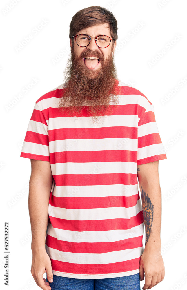 Obraz premium Handsome young red head man with long beard wearing casual clothes sticking tongue out happy with funny expression. emotion concept.