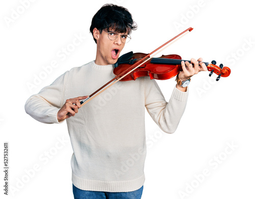 Handsome hipster young man playing violin in shock face, looking skeptical and sarcastic, surprised with open mouth