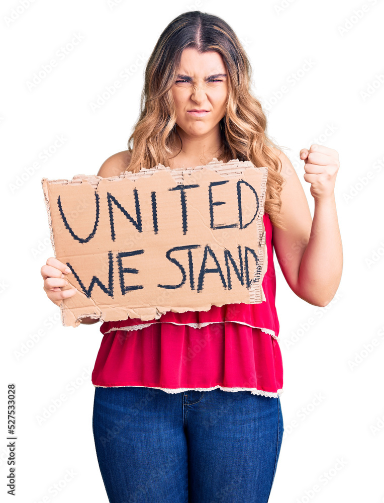Young caucasian woman holding united we stand banner annoyed and frustrated shouting with anger, yelling crazy with anger and hand raised Young caucasian woman holding united we stand banner annoyed and frustrated shouting with anger, yelling crazy with anger and hand raised