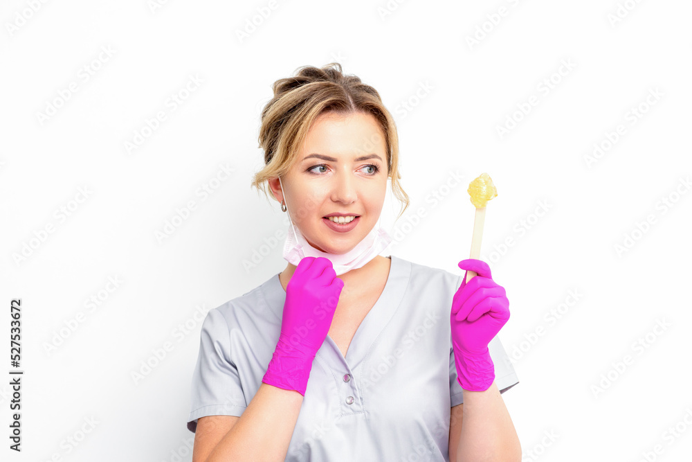 The master of sugar hair removal holds liquid yellow sugar paste, wax for depilation on a wooden stick on a white background The master of sugar hair removal holds liquid yellow sugar paste, wax for depilation on a wooden stick on a white background